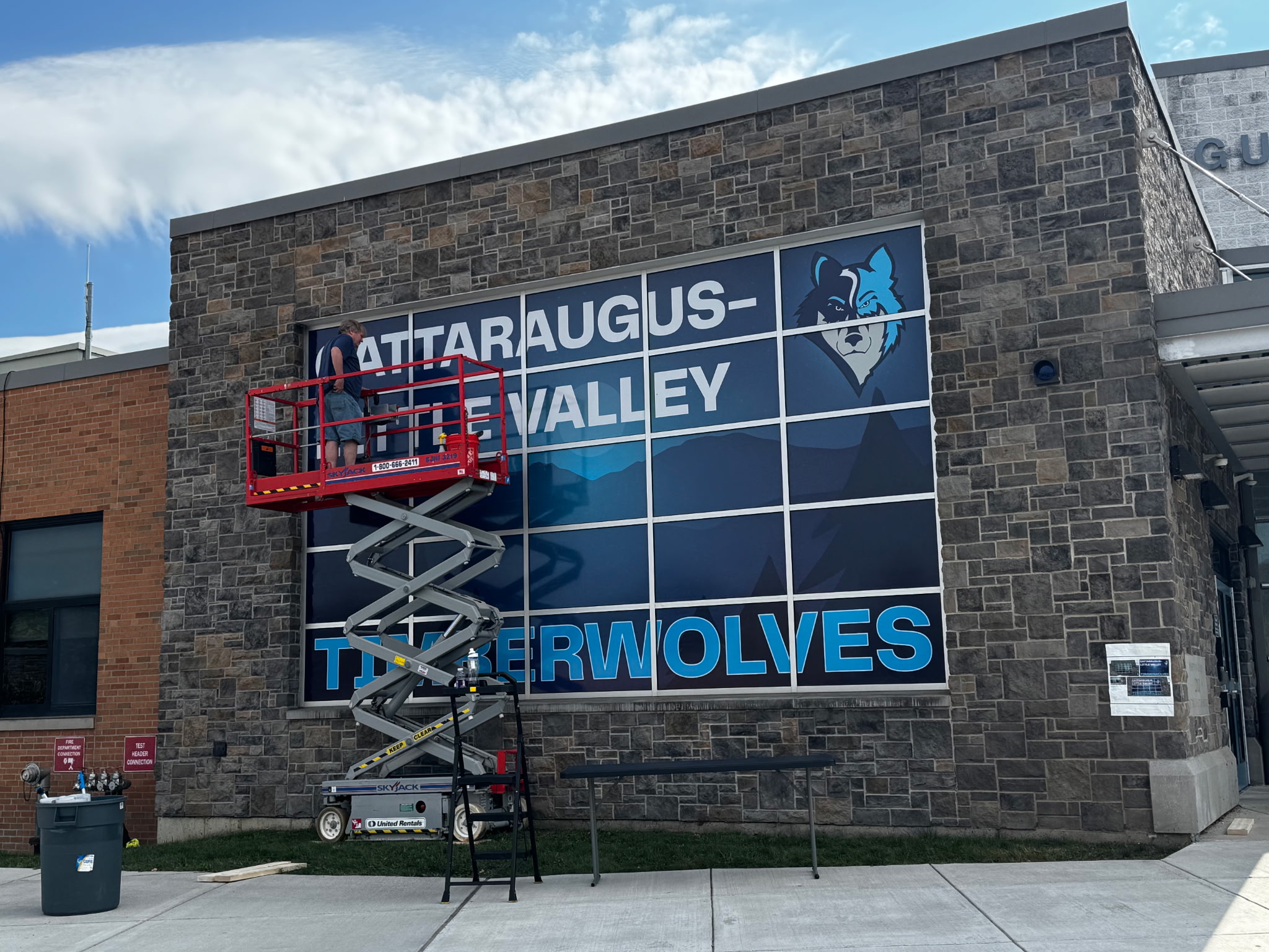 Workers installing vinyl design on window featuring  Cattaraugus Little Valley High School Timberwolves logo and colors.